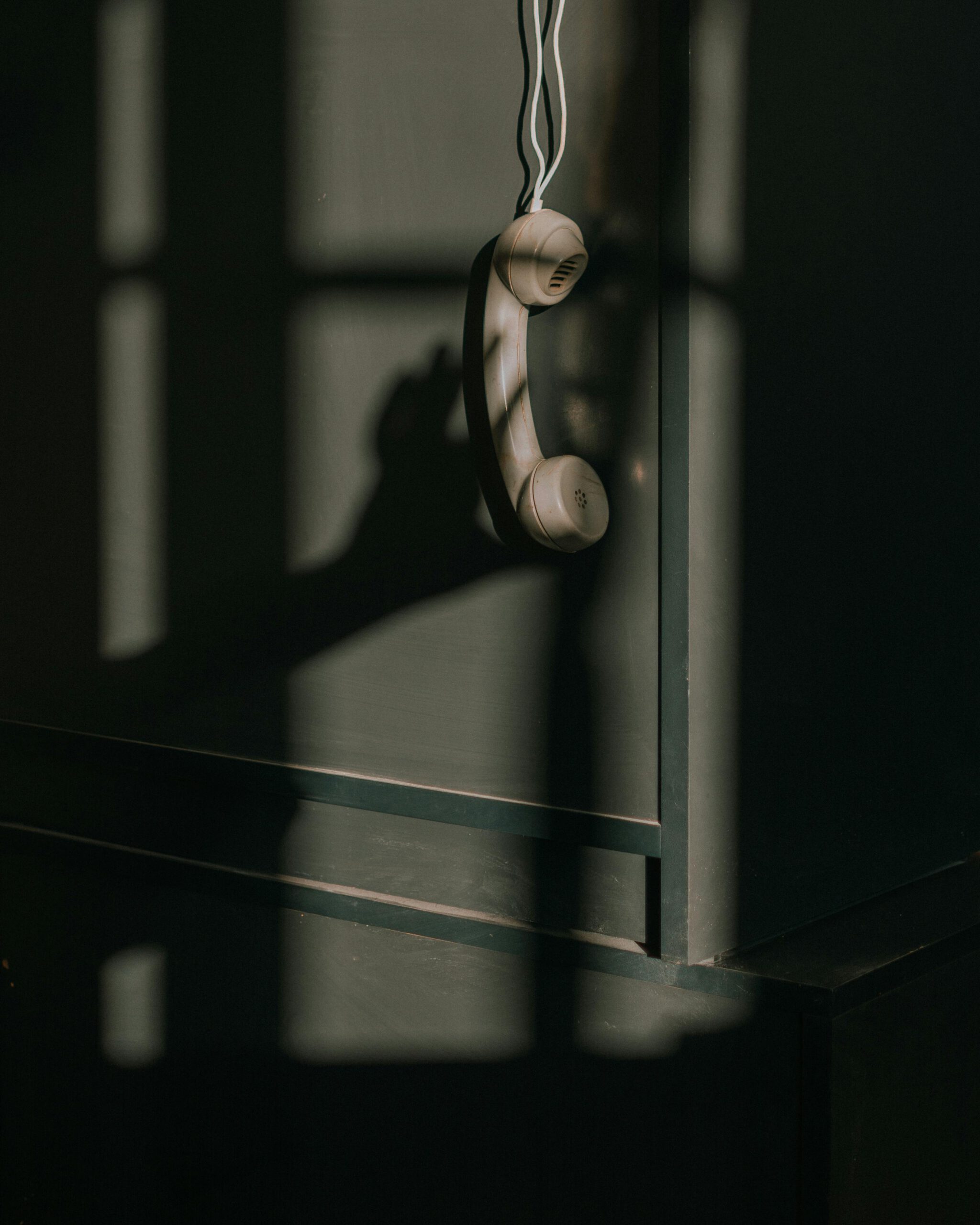 Home A vintage telephone handset hangs against a wall with dramatic lighting and shadows.